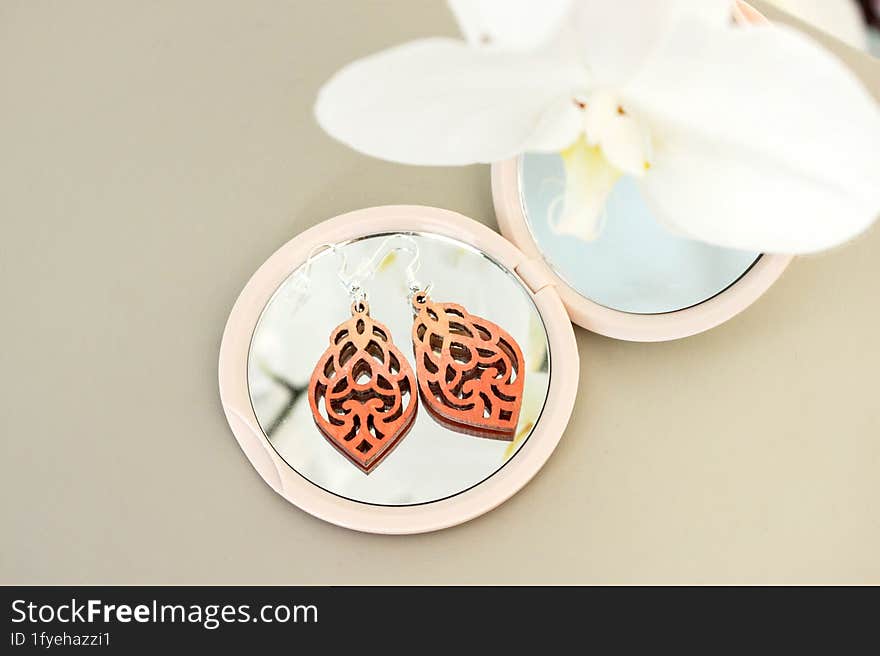 Earrings on mirrorr. Orchis flower and accessory with a mirror reflection of the beautiful blue sky in the morning