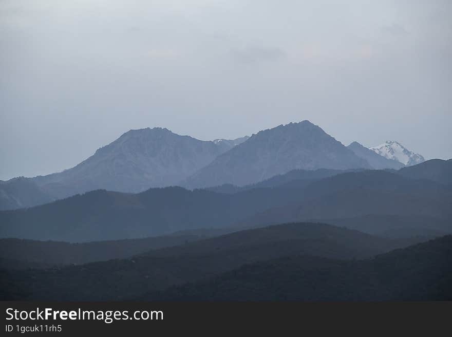 Landscape of the Trans-Ili Alatau mountains on an early cloudy morning in thick morning fog, haze