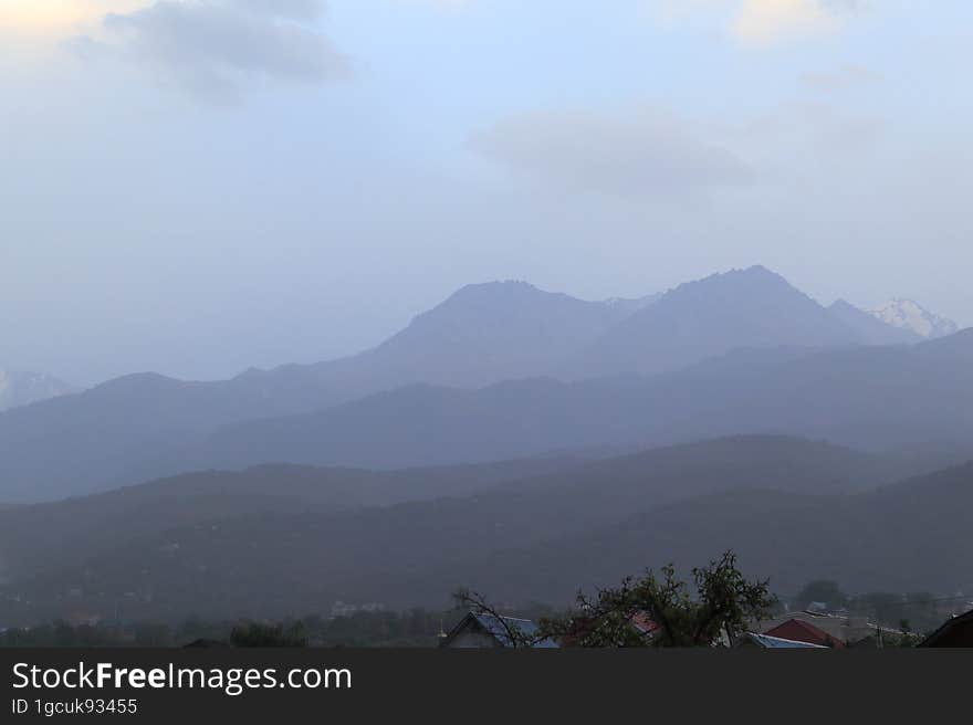 Mountains of Trans-Ili Alatau on an early cloudy morning in the morning fog during sunrise over the suburbs