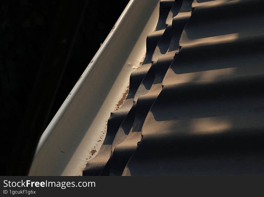 A dark blue roof next to a white roof drain, illuminated by the setting sun during sunset