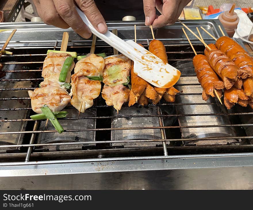 The hands of a man selling grilled sausages are spreading butter on grilled sausages