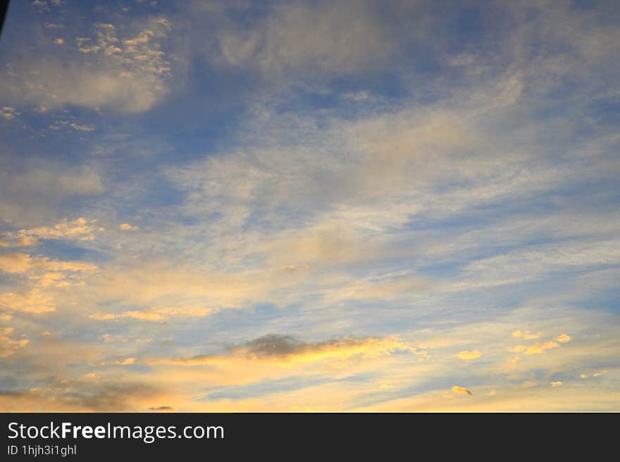 Beautiful cirrus and small cumulus clouds of yellow and orange colors in the blue sky illuminated by the morning sun rays