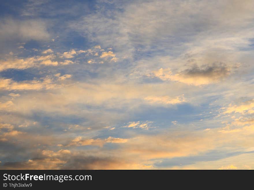 Beautiful cirrus and small cumulus clouds of yellow and orange colors in the blue sky illuminated by the morning sun rays