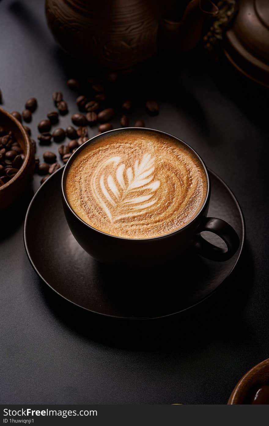 Close-up of a black coffee cup on a black background with copper pots and roasted coffee beans