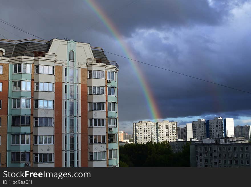 Landscape with a panel high-rise house on a dark sky with a rainbow. Double rainbow in the dark sky. A storm cloud over the city.