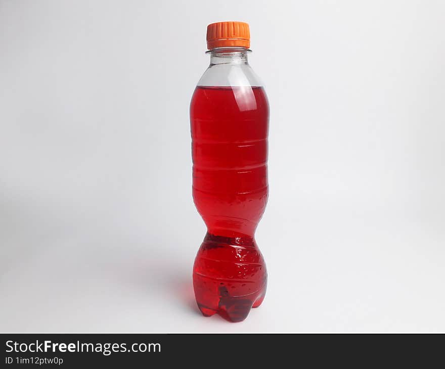 a bottle containing a red soda drink and a white background