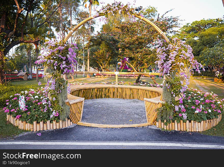 This Enchanting Garden Scene Showcases a Captivating Floral Archway, Inviting Viewers into a Lush Oasis. Adorned with Vibrant Purple Blooms and Nestled Amidst a Tranquil Park Setting, This Installation Blends Rustic Charm with Natural Beauty. the Bamboo Framing Adds an Eco-Friendly Touch, Enhancing the Organic Appeal of the Display.