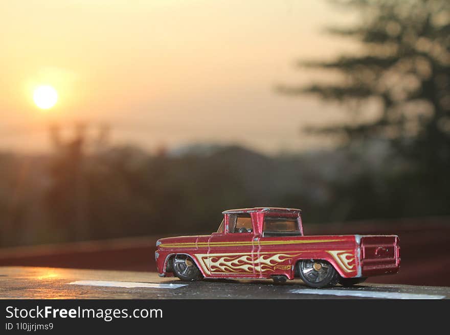 A toy car placed on a wooden block painted to resemble a highway with a morning scene in the background.