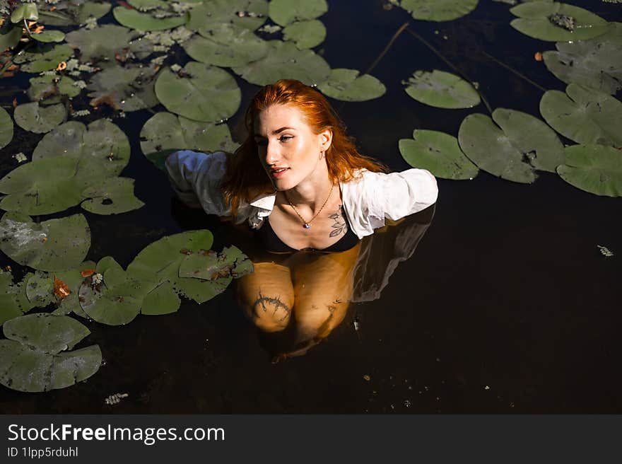 Red hair woman swimming in summer lake with lily