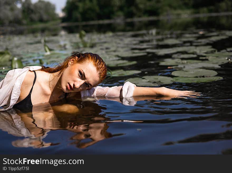 Red hair woman swimming in summer lake with lily