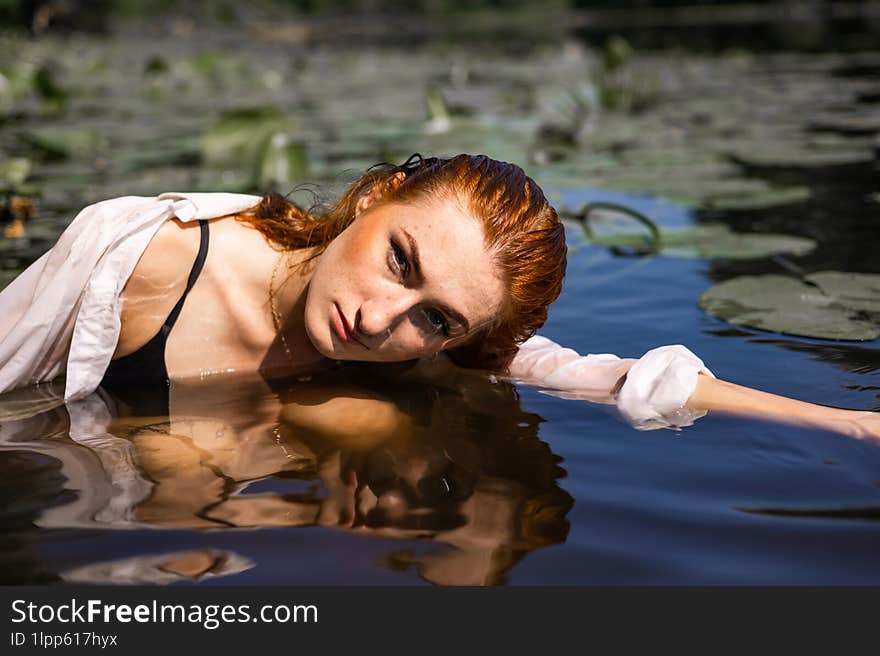 Red hair woman swimming in summer lake with lily