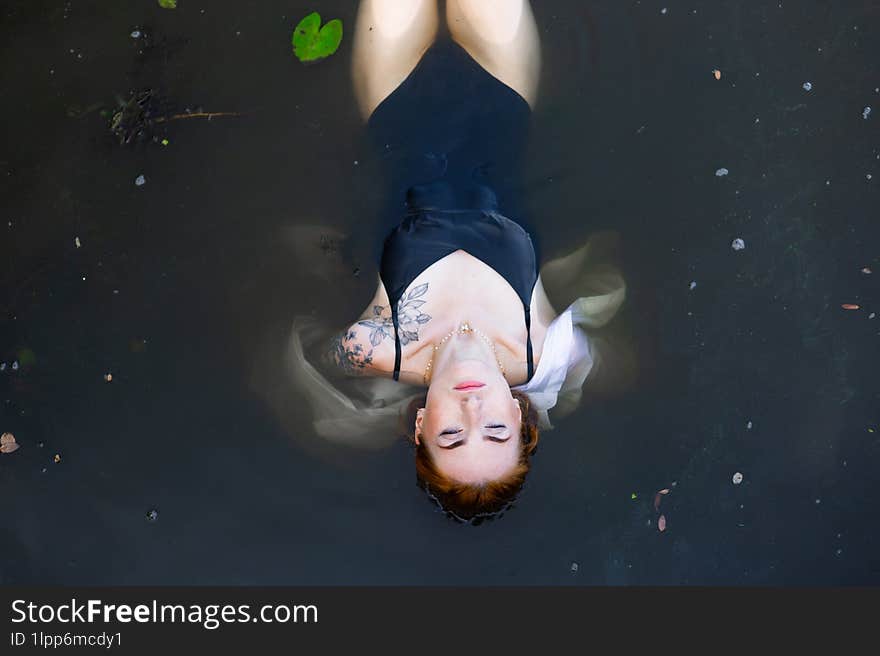 Red hair woman swimming in summer lake with lily