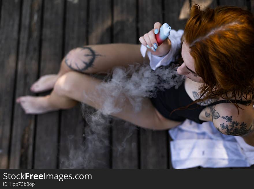 Red hair woman in swimsuit smoking on wooden bridge near lake.