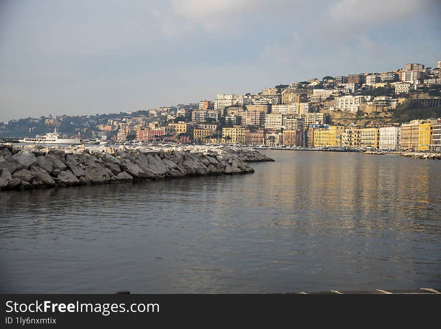 Protective breakwater rocks in naples, italy reflect colorful buildings in calm mediterranean waters, creating a picturesque cityscape popular with tourists. Protective breakwater rocks in naples, italy reflect colorful buildings in calm mediterranean waters, creating a picturesque cityscape popular with tourists