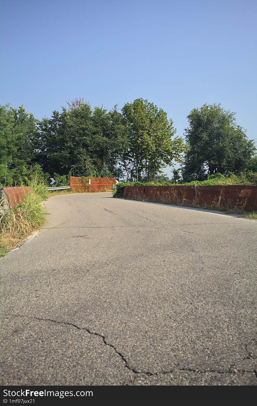 Country road passing over a brook next to trees and fields on a summer day in the italian countryside. Country road passing over a brook next to trees and fields on a summer day in the italian countryside