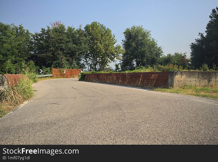 Country road passing over a brook next to trees and fields on a summer day in the italian countryside. Country road passing over a brook next to trees and fields on a summer day in the italian countryside