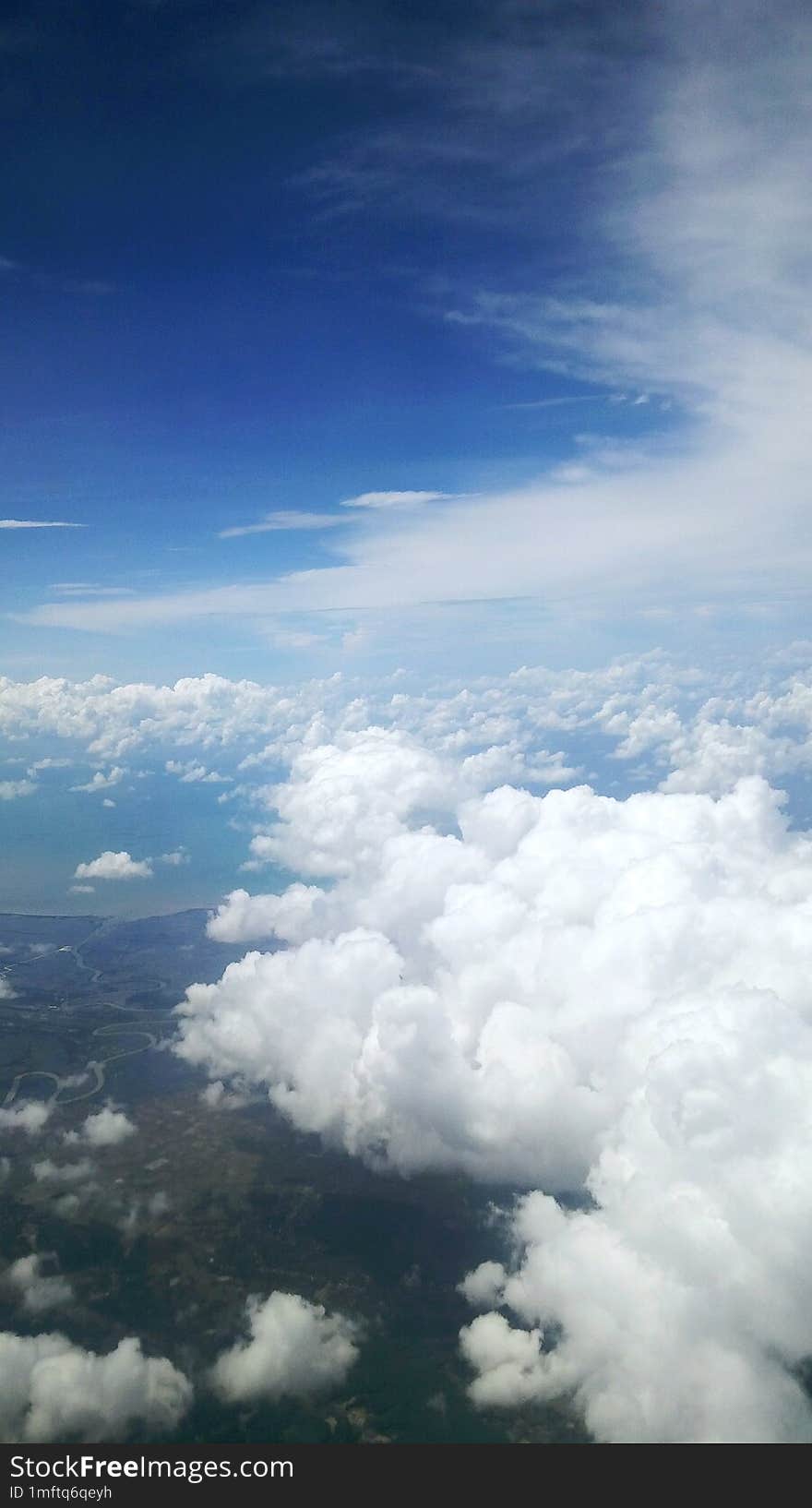 The view in bright daylight seen from inside the plane is of sky, clouds and land.