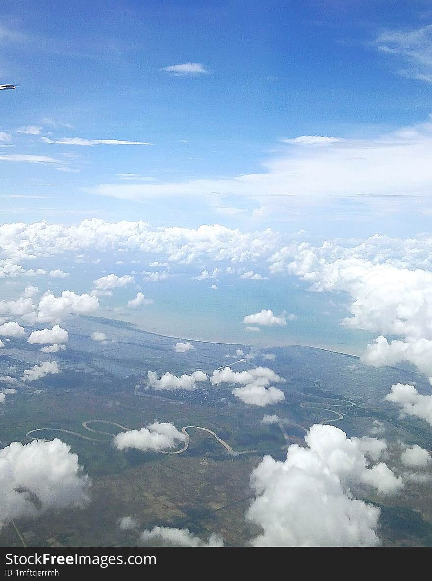 The View In Bright Daylight Seen From Inside The Plane Is Of Sky, Clouds And Land.