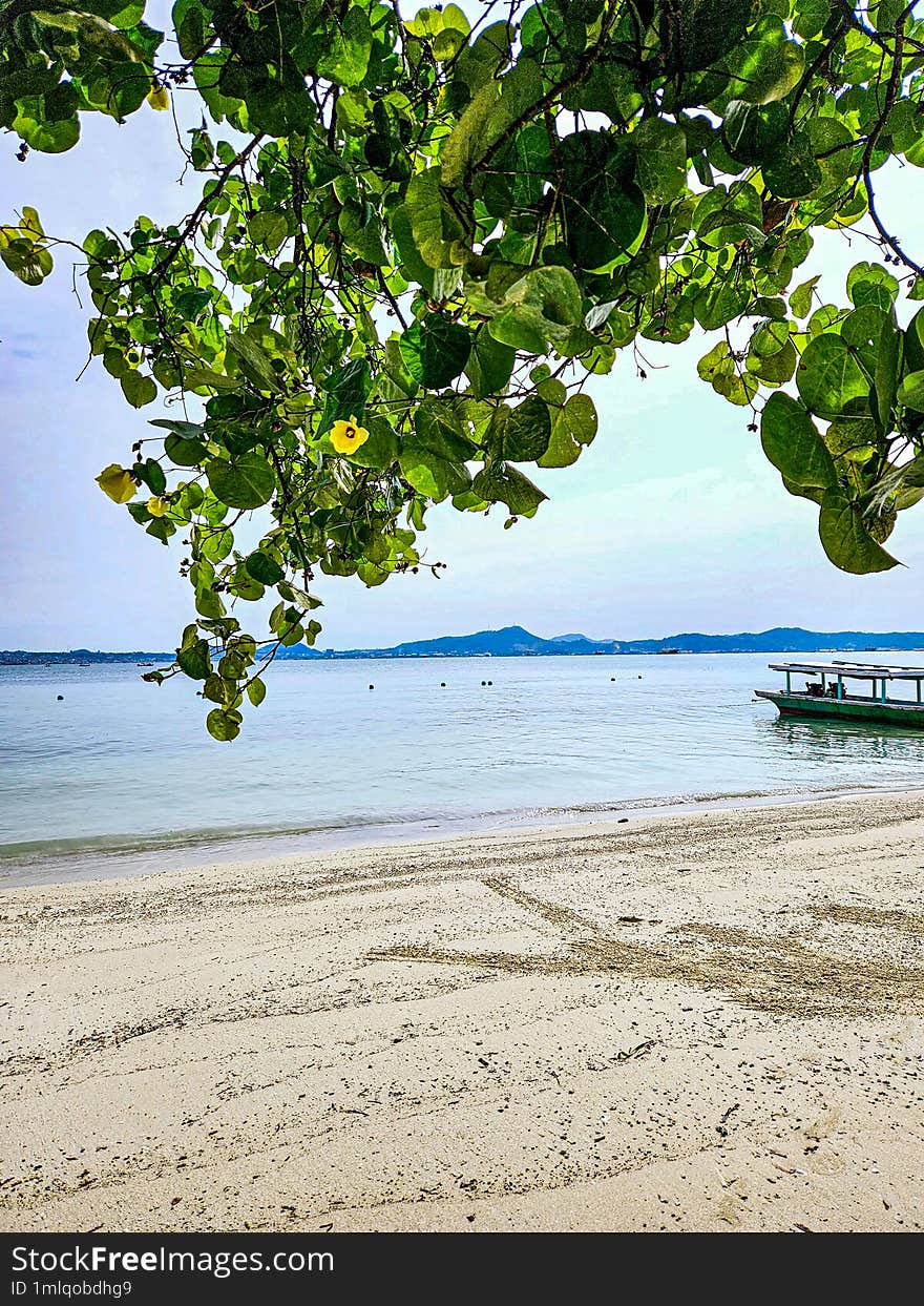 View of the beach and boats in Lampung Bay, Indonesia with hills in the background.