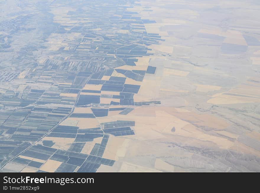 Aerial view of a vast landscape with a patchwork of agricultural fields in various shapes and shades, highlighting the human impact on natural terrain.