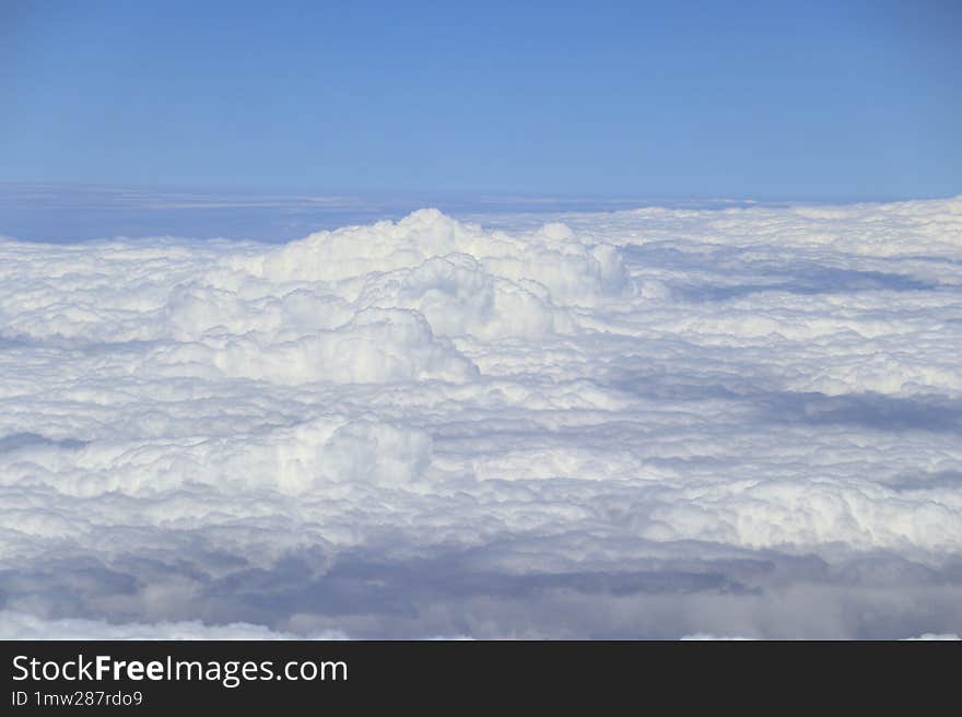 View from above the fluffy, dense clouds, with a clear, deep blue sky indicating fair weather, taken from an aircraft