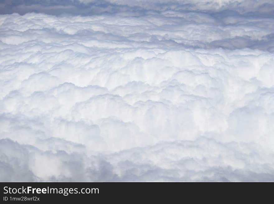 View from above the fluffy, dense clouds, with a clear, deep blue sky indicating fair weather, taken from an aircraft