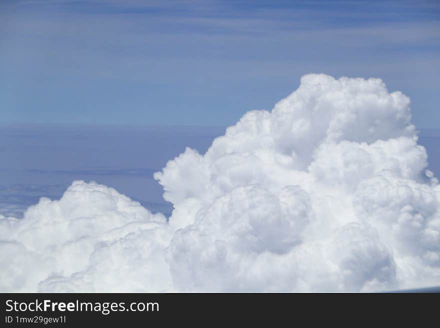 View from above the fluffy, dense clouds, with a clear, deep blue sky indicating fair weather, taken from an aircraft