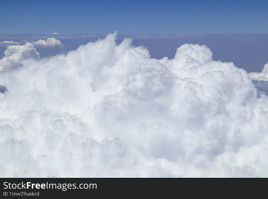 View from above the fluffy, dense clouds, with a clear, deep blue sky indicating fair weather, taken from an aircraft