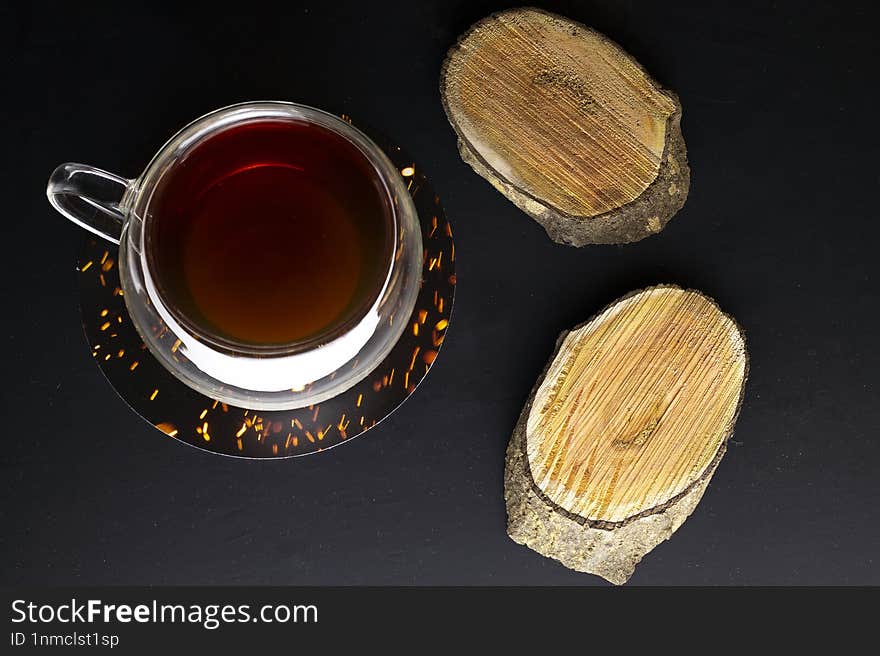 Top view of black mug with tea on black background with wooden coasters near mug