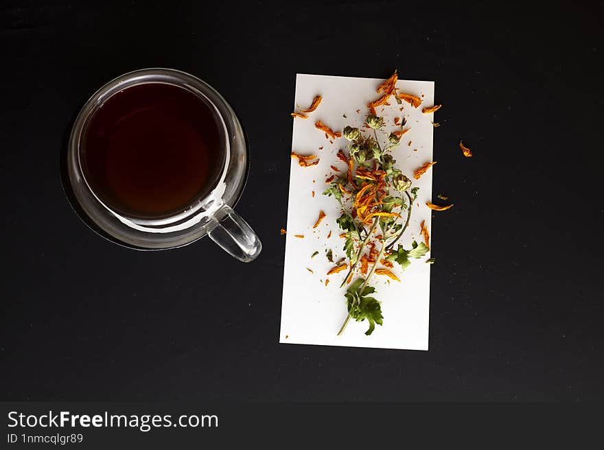 Top view of black mug with tea on black background with dried flower near mug