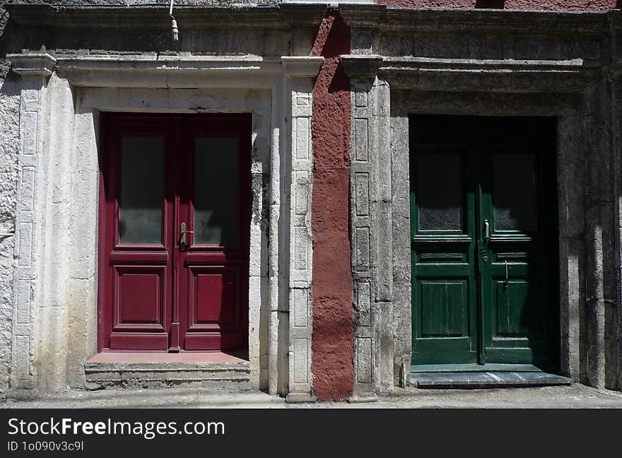 Two double doors with stone surrounds, one painted a deep red color and the other a dark green