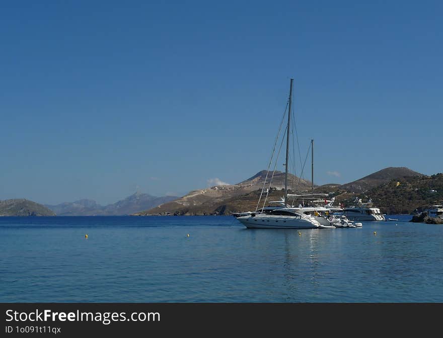 During summer time several yachts are moored in the calm, blue waters of the greek islands under the clear, blue, summer sky of Greece. During summer time several yachts are moored in the calm, blue waters of the greek islands under the clear, blue, summer sky of Greece
