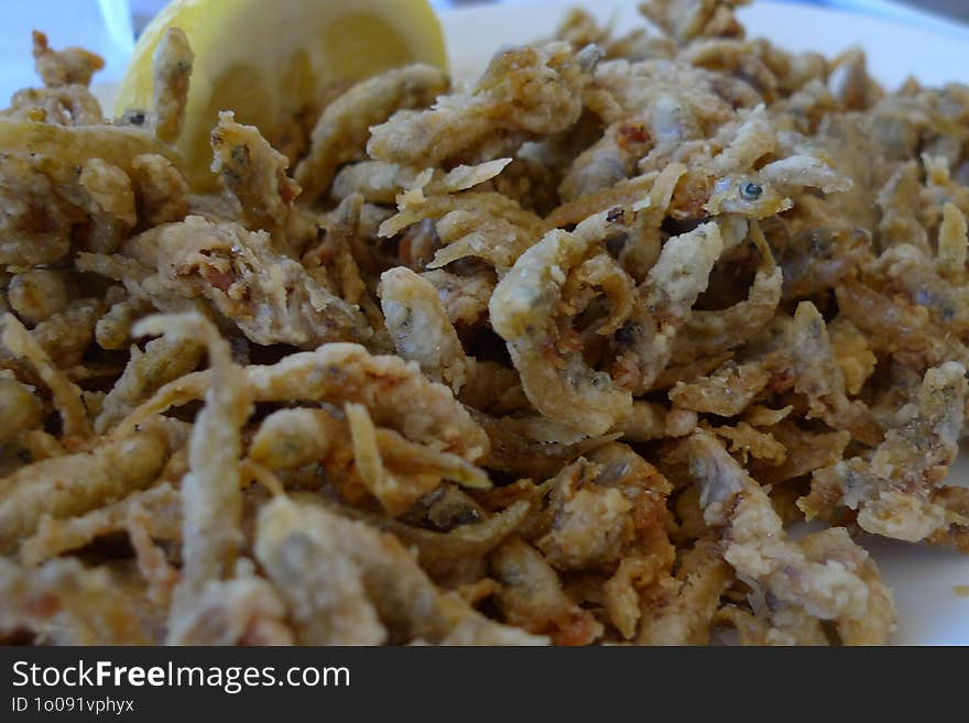 A close-up view of a serving of small, deep-fried fish, commonly known as fish fritters, served with a wedge of lemon