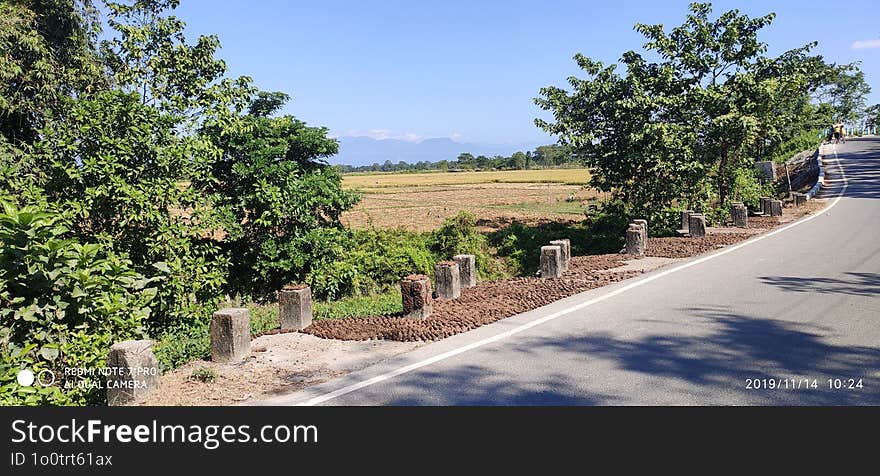 Winding Country Road Through Lush Green Fields, Leading To Distant Mountains Under A Clear Blue Sky