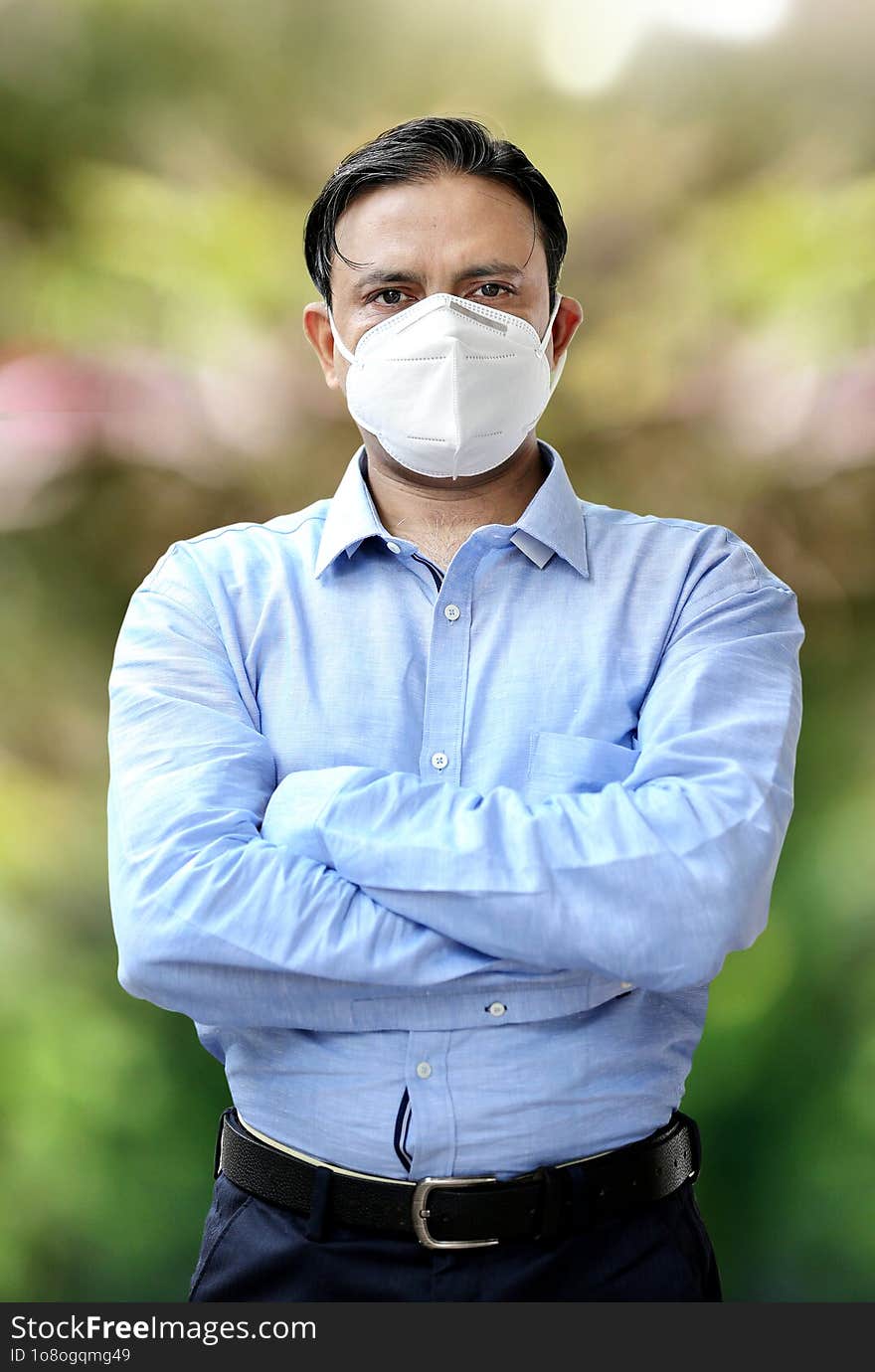 Young Indian confident businessman in mask standing outdoors.