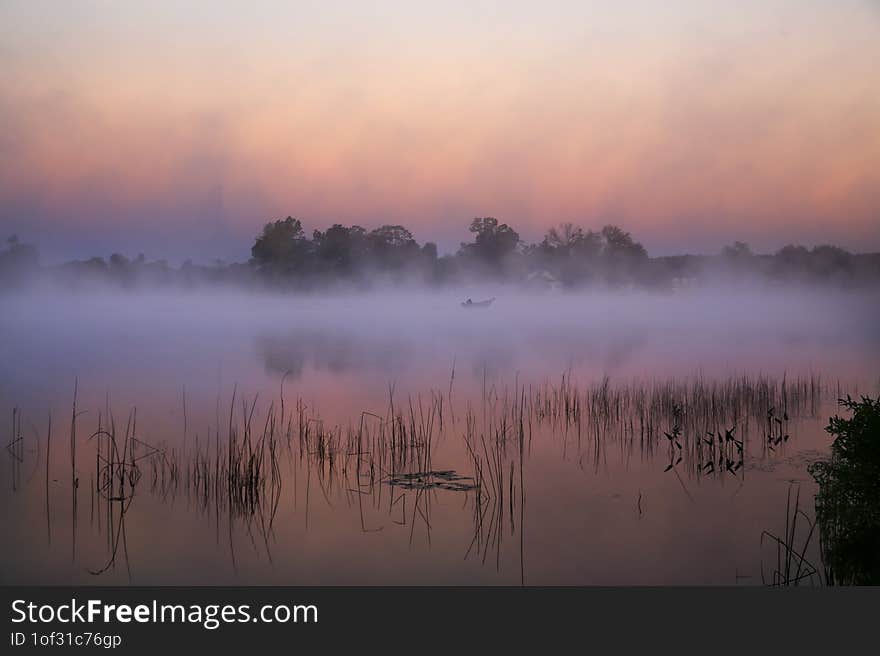 A lone fisherman in a small boat fishing on an inland lake on a foggy morning