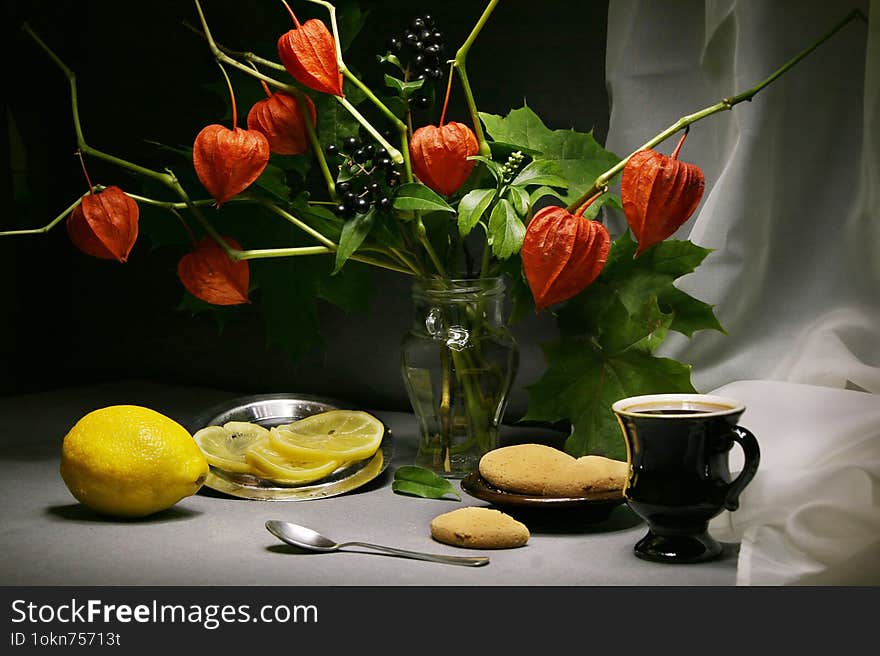 Still life with a bouquet of autumn leaves and physalis, a cup of coffee with cookies and lemon