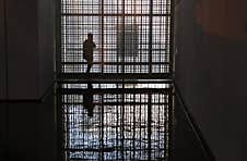 Solitary Figure Is Silhouetted Against A Geometric Patterned Glass Wall In The Dark, Reflected Perfectly On The Glossy Floor Royalty Free Stock Photography