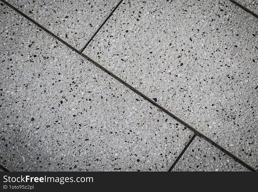 Close-up view of a terrazzo floor composed of light-colored tiles with dark speckles, divided by thin, dark grout lines