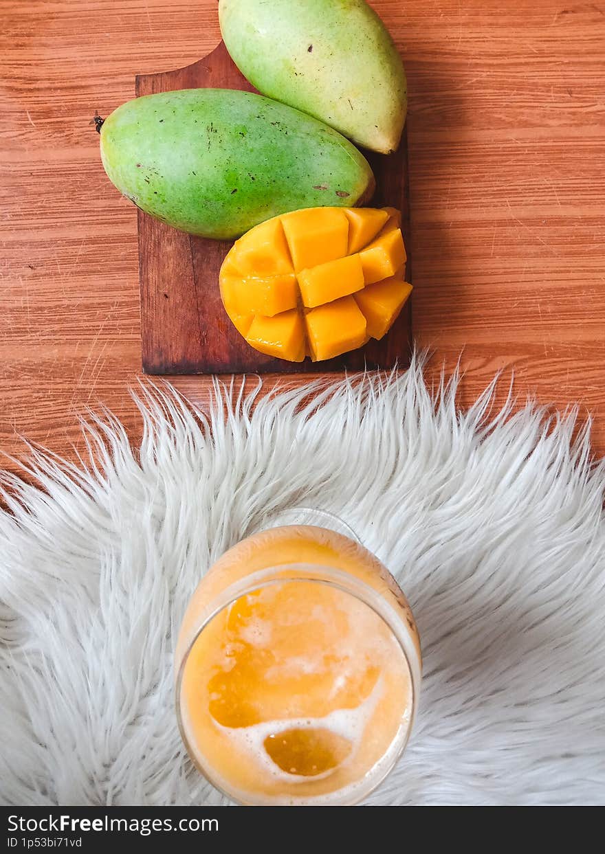 The sweet and fresh mango juice was served in a fancy glass, while next to it was 1 peeled mango and 2 others still intact.