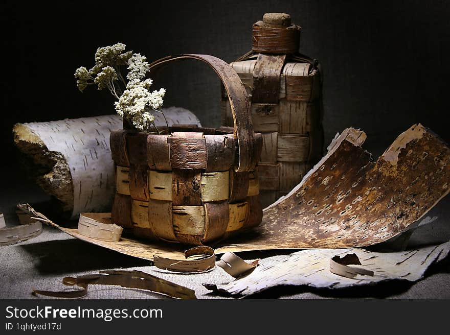 Still life with a birch bark basket and bottle surrounded by scattered birch bark