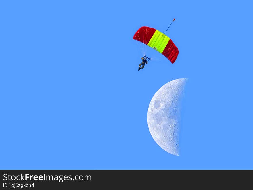 Skydiver descends from the sky on a multi-colored parachute against the backdrop of the Moon