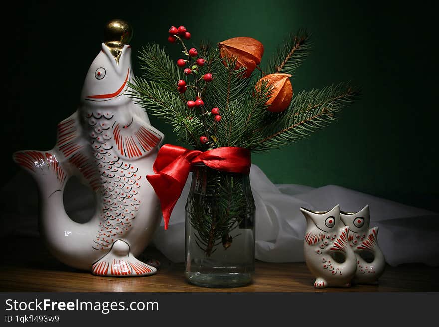 The branches of the fir tree, gathered into a bouquet, stand in a vase on the table, decorated with berries. And ceramic fish are