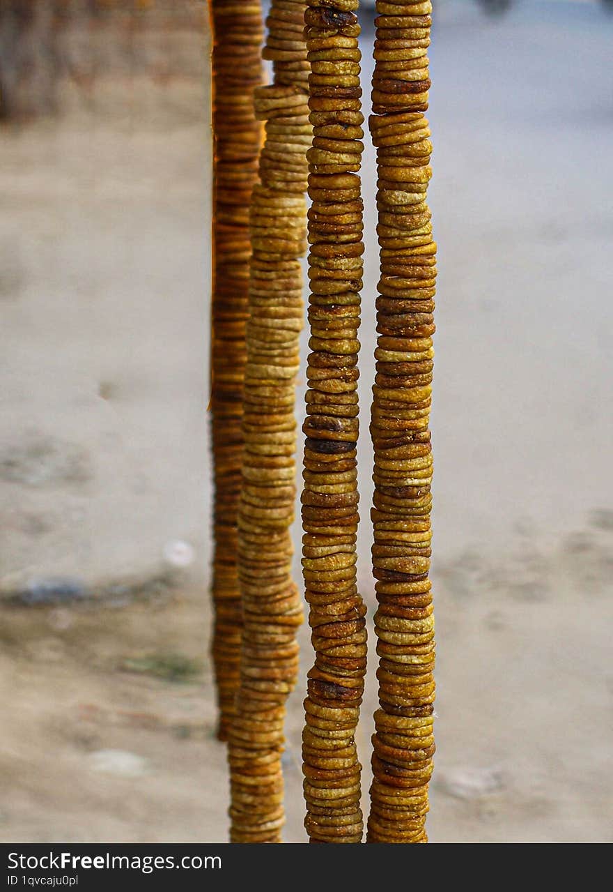 A close-up image of dried figs hanging in long, vertical strings. The figs are arranged in a circular pattern, creating a visually