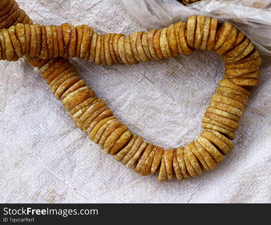 A close-up image of a long string of dried figs. The figs are arranged in a circular pattern, creating a visually appealing displa