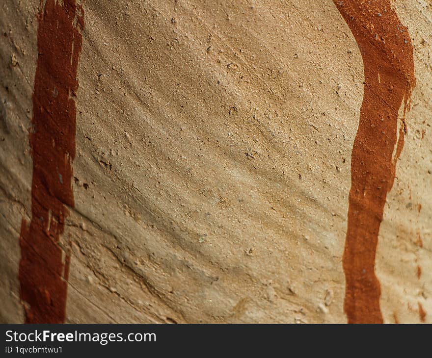 A close-up of a textured surface with a mix of brown and tan colors. The surface has a rough, almost sandy texture with prominent vertical and horizontal lines in a darker shade of brown.