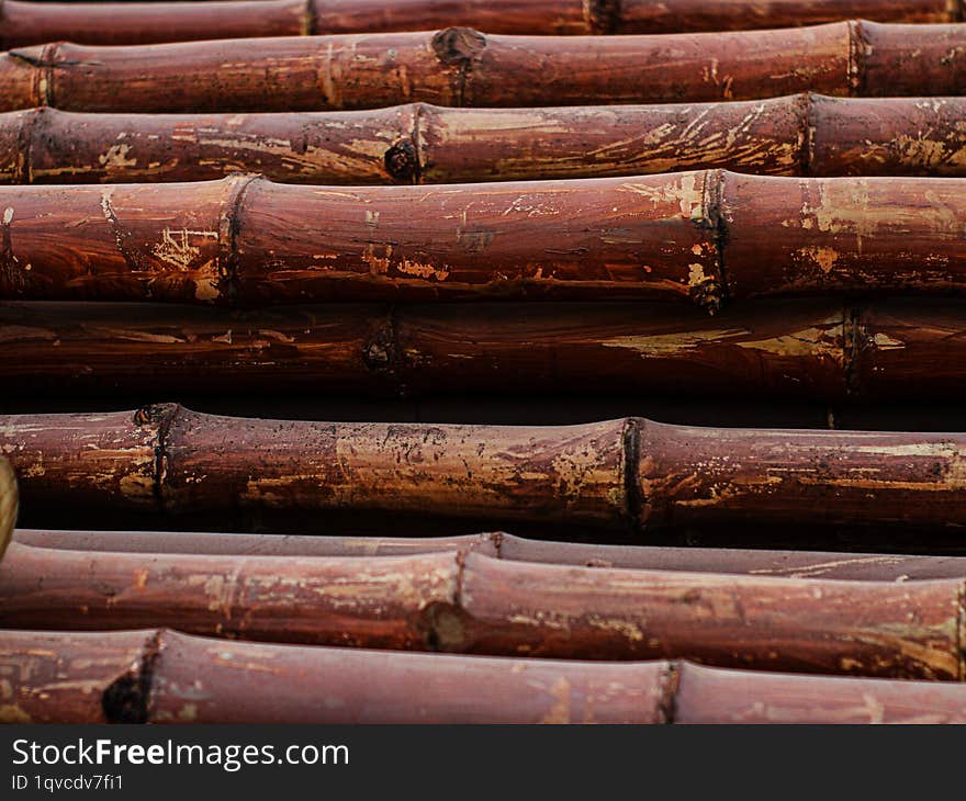 A close-up photograph of a stack of weathered bamboo poles. The bamboo is a rich reddish-brown color with visible signs of wear an