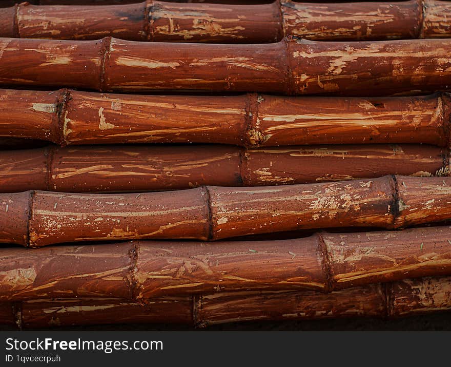 A close-up photograph of a stack of weathered bamboo poles. The bamboo is a rich reddish-brown color with visible signs of wear an