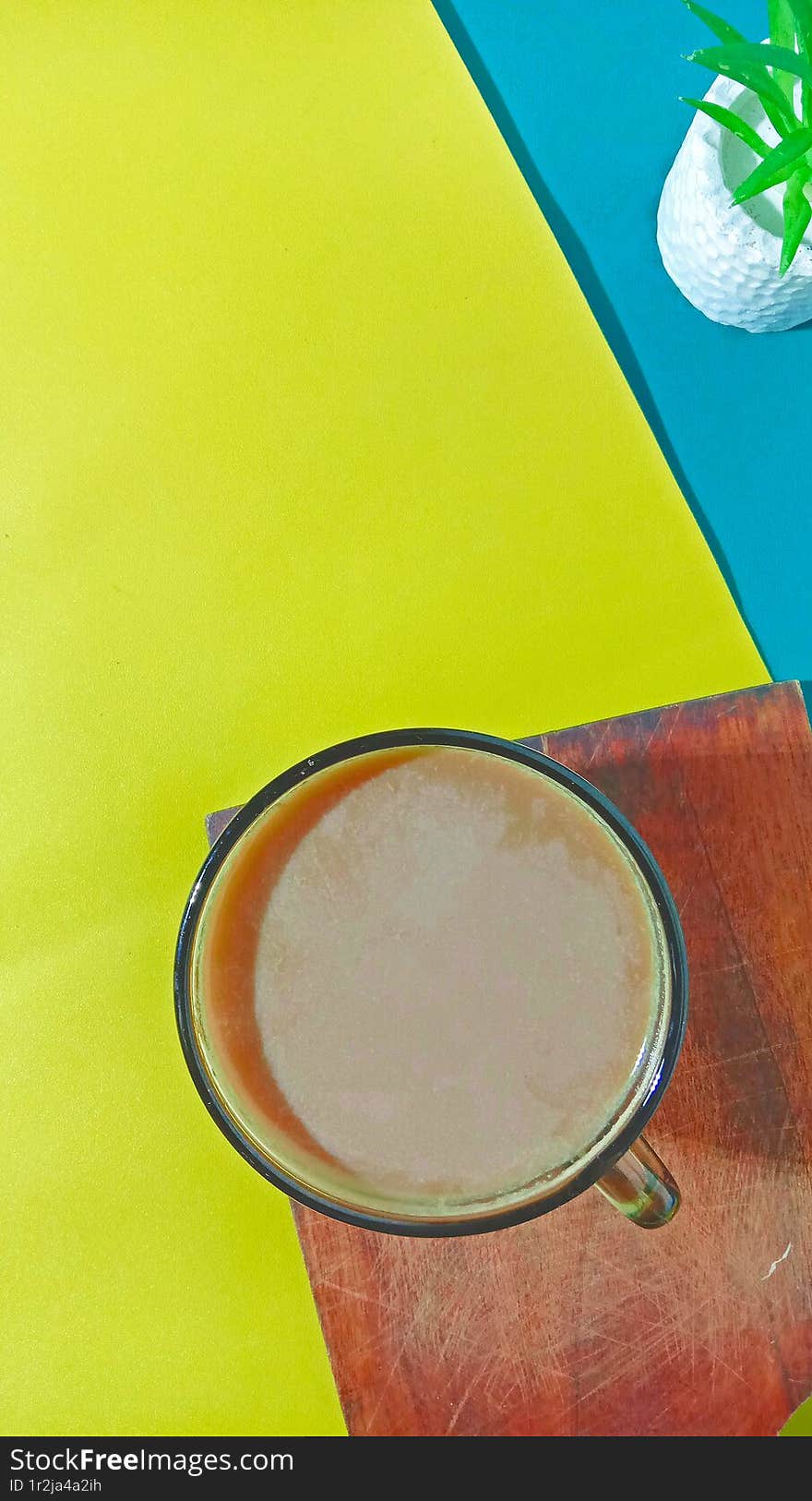 A cup of hot milk coffee placed on a cutting board with a double-colored background, top view, vertical shot, still life and flat