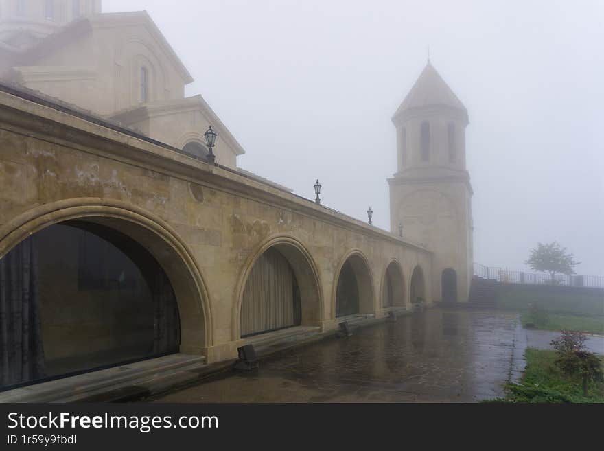 Tiled church courtyard, lower part with rooms, bell tower in the fog